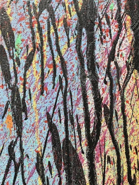 An abstract painting featuring a vibrant background filled with splatters of blue, pink, orange, and other colors. Large, bold black streaks and drips are layered over the colorful backdrop, creating a striking contrast.