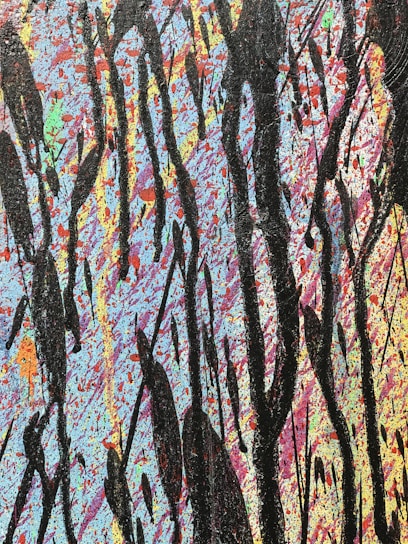 An abstract painting featuring a vibrant background filled with splatters of blue, pink, orange, and other colors. Large, bold black streaks and drips are layered over the colorful backdrop, creating a striking contrast.