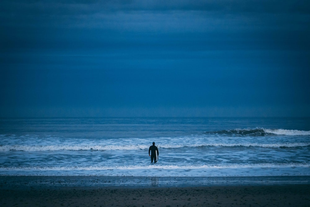 man standing on beach under cloudy sky