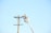 A worker in a bucket lift is performing maintenance on a utility pole, wearing protective gear including a hard hat. The utility pole has multiple wires attached, and the scene is set against a clear blue sky.