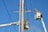 Two utility workers in safety gear are using bucket trucks to work on a power line. The sky is clear and blue, providing a backdrop to the scene. Both workers are elevated in their respective buckets, focusing on tasks related to the maintenance or repair of the electrical infrastructure.