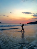 Sunset silhouette of a surfer carrying a board along the shoreline