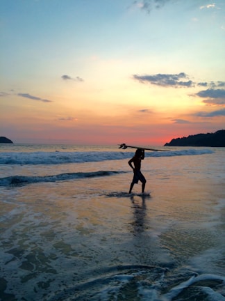 Sunset silhouette of a surfer carrying a board along the shoreline