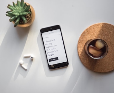 post-2014 iPhone beside Apple AirPods and succulent plant on white surface