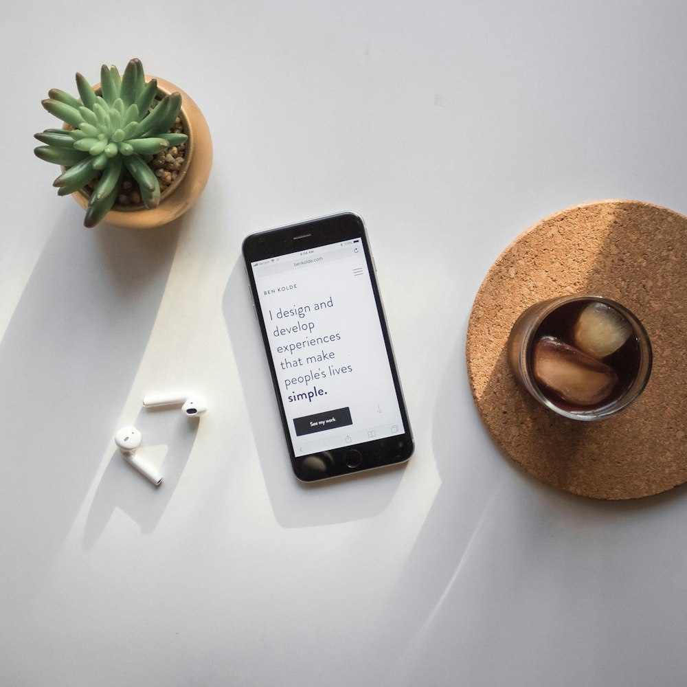 post-2014 iPhone beside Apple AirPods and succulent plant on white surface