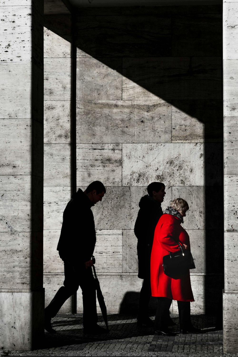 two men and woman walking beside gray concrete wall with sahdow