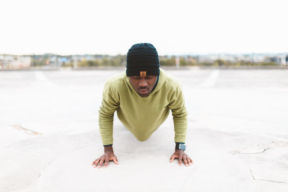 man in green long-sleeved shirt doing a push-up on gray concrete pavement