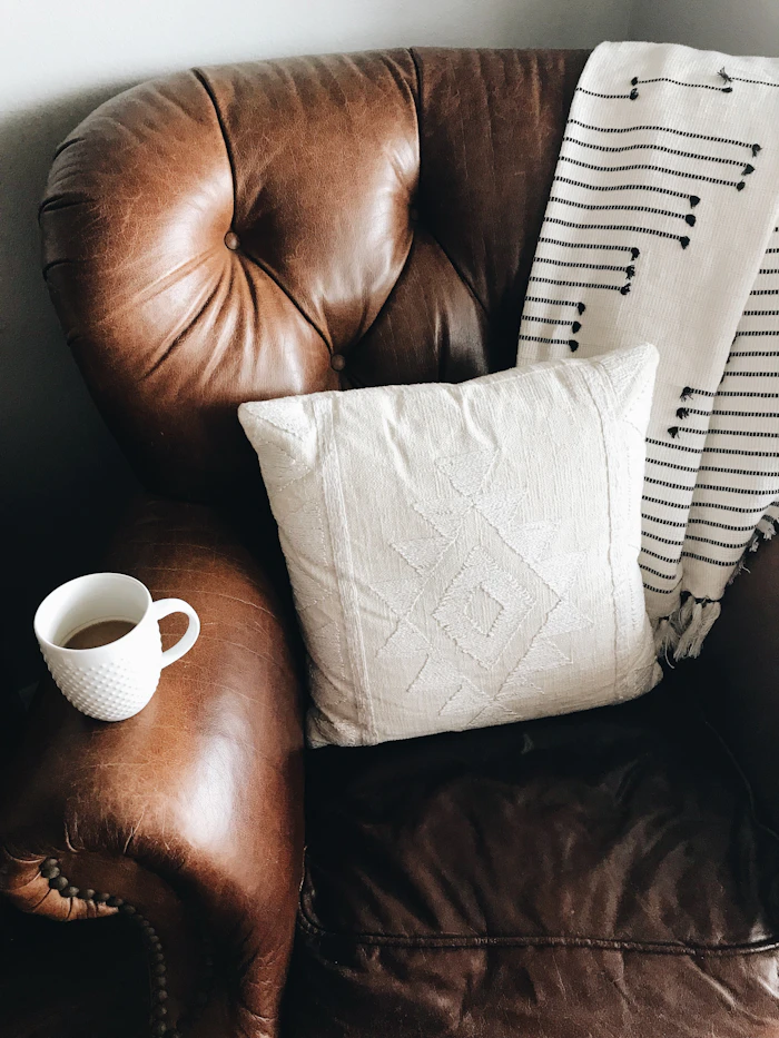 A handwoven white cotton cushion cover styled on a brown leather armchair
