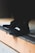 A close-up view of black athletic shoes with a visible brand logo, placed on a concrete step. The shoes are stylishly designed and appear to be suitable for sports or casual wear. The background is blurred, focusing attention on the footwear.