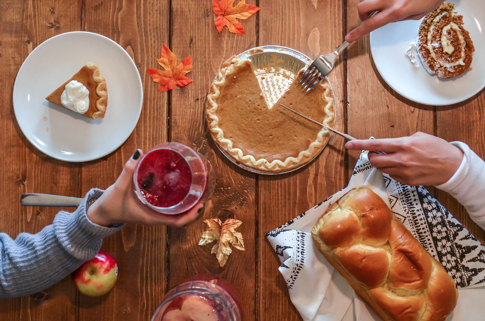 A person cutting a slice from a pie on a table beside bread