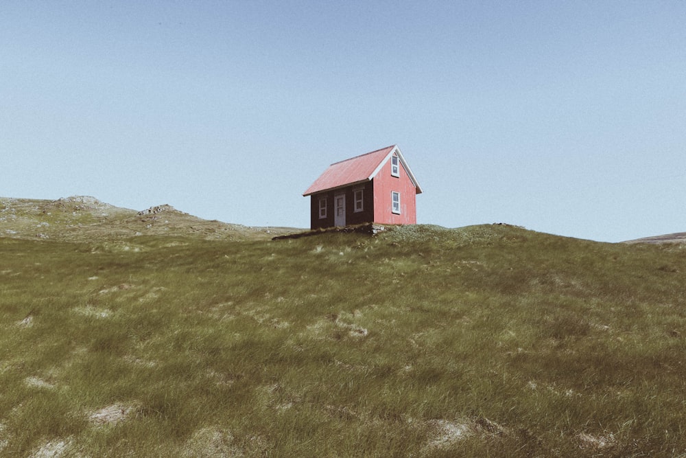 昼間の青空の下、丘の上の赤い木造の小屋