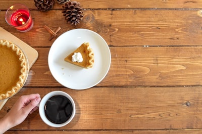 slice of pie with whipped cream on ceramic plate near coffee pumpkin pie zoom background