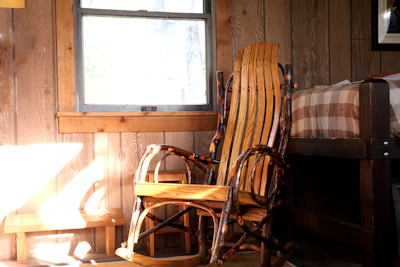 A cozy rustic wooden rocking chair nestled on a sunlit patio surrounded by greenery.