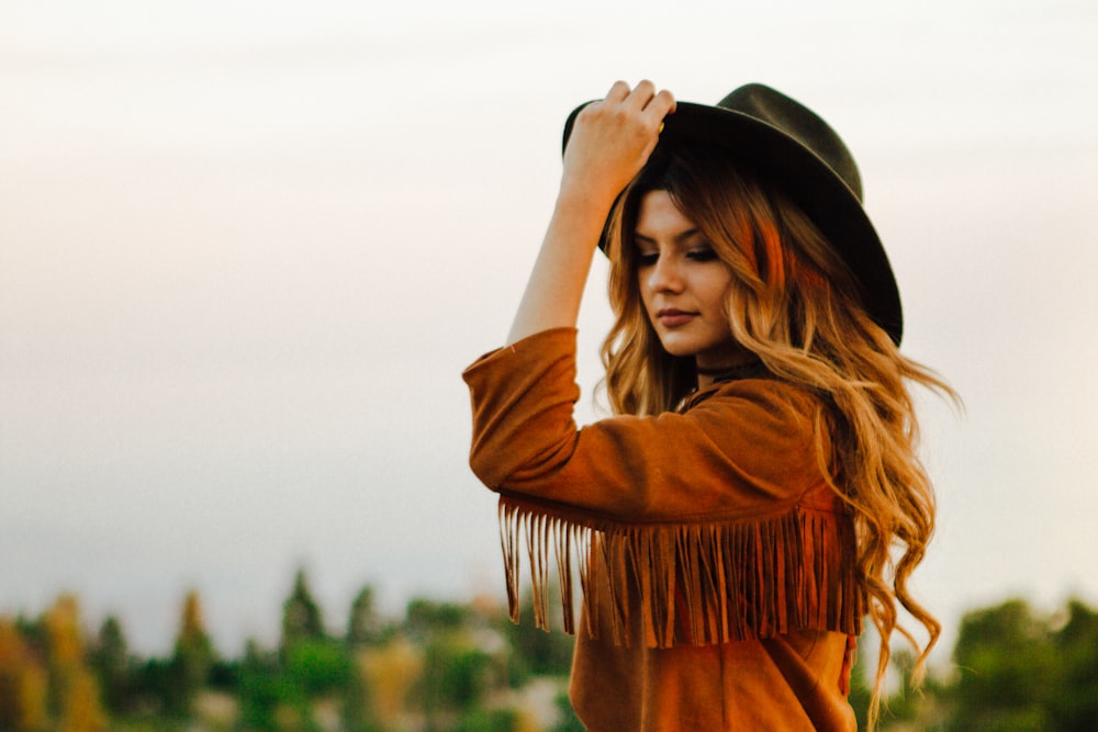 Donna che indossa una giacca marrone con frangia che tiene il cappello durante il giorno