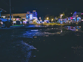 A nighttime cityscape with glowing streetlights and reflections on wet pavement.