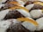 A close-up view of multiple pastries topped with white cream filling and garnished with slices of candied orange peel. The pastries have a dusting of powdered sugar, and the texture of the pastry is flaky and golden brown.