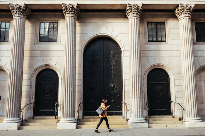 A woman walks past a white building with tall ionic columns