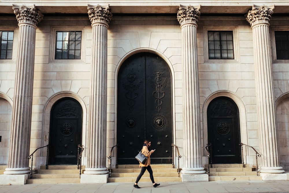 mujer caminando frente a un edificio blanco con pilares iónicos