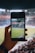 A cricket fan cheering in a stadium, holding a smartphone displaying live scores.