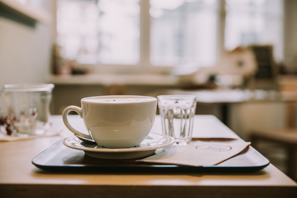 taza de té de cerámica blanca en platillo de cerámica blanca dentro de la habitación con ventanas de vidrio