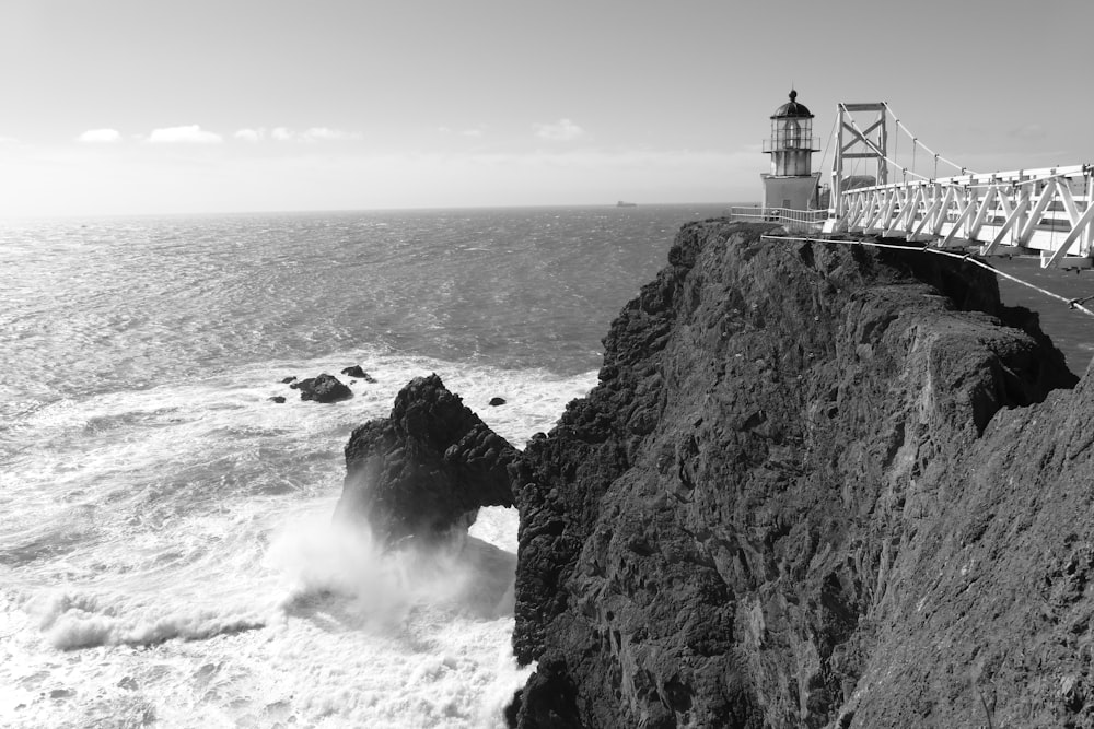 greyscale photography of lighthouse near bridge