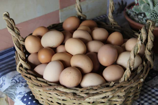 A rustic basket filled with fresh organic eggs nestled in straw on a wooden table.