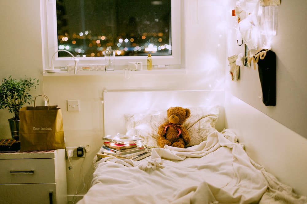 osito de peluche en la cama cerca de la mesita de noche y la ventana