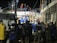 A group of people, including some wearing uniforms labeled 'MARINA,' are gathered around a partially collapsed structure at night. Many are wearing safety helmets and other protective gear, suggesting an emergency response or rescue operation. The scene is illuminated by artificial lighting, and some individuals are on top of the debris while others are standing nearby.