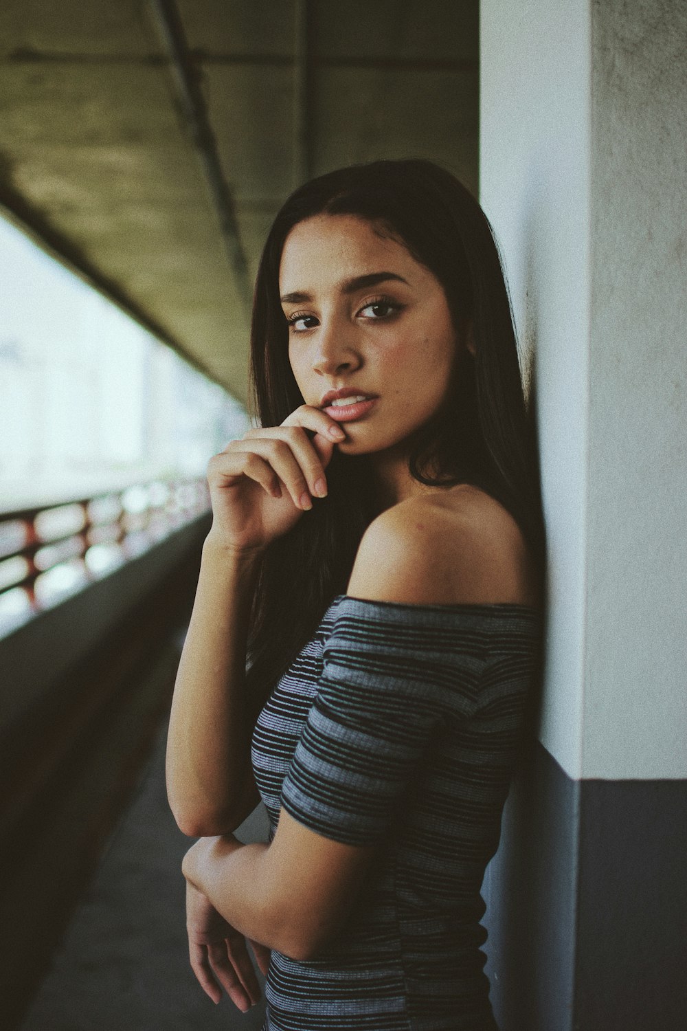 woman in gray off-shoulder top shirt leaning on white wall