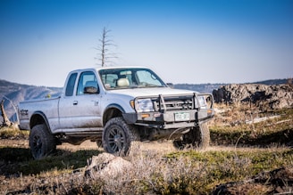 A rugged pickup truck loaded with oilfield tools parked near drilling rigs under a wide West Texas sky.