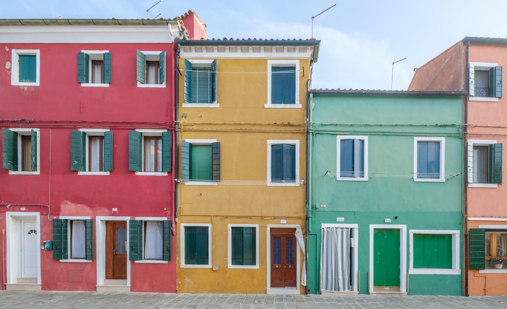 três casas de concreto de cores variadas sob o céu azul e branco durante o dia