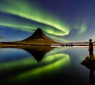 man standing beside the body of water with Aurora lights in the sky
