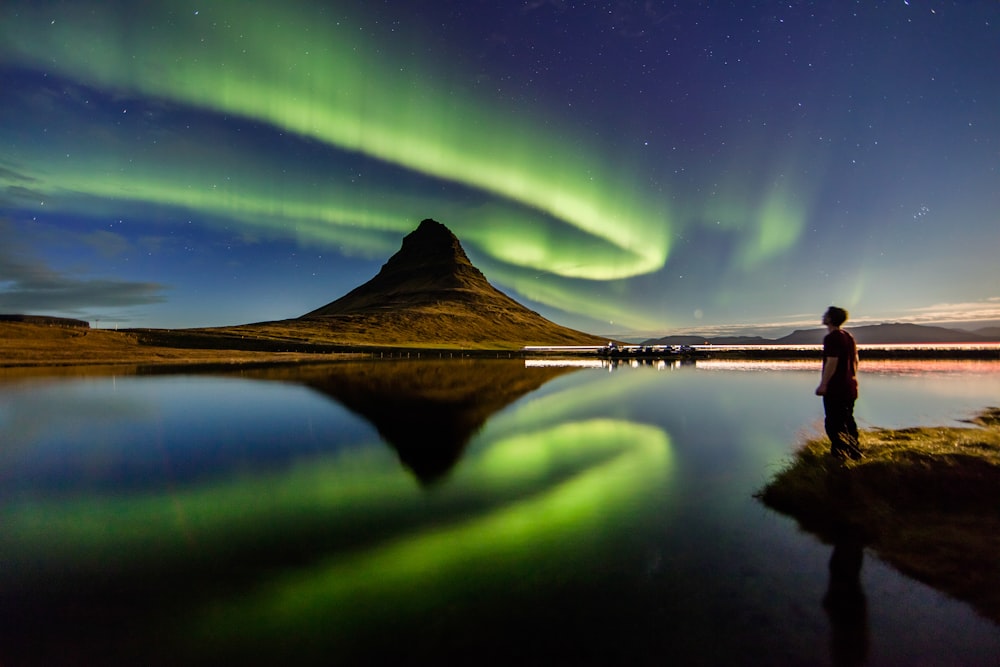 uomo in piedi accanto allo specchio d'acqua con le luci dell'aurora nel cielo