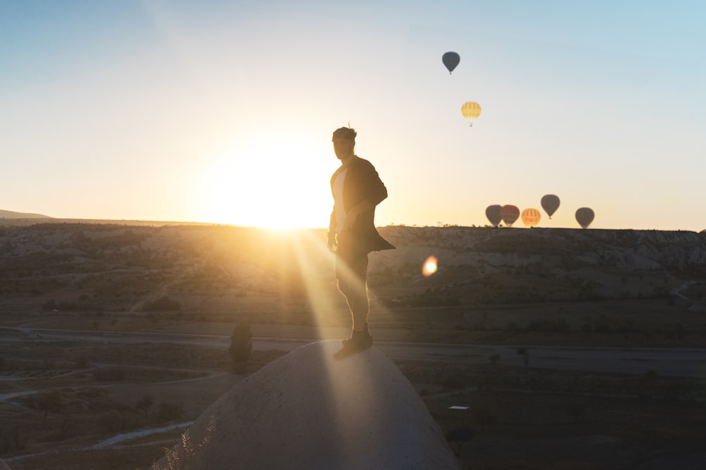 a man standing on top of a rock next to hot air balloons