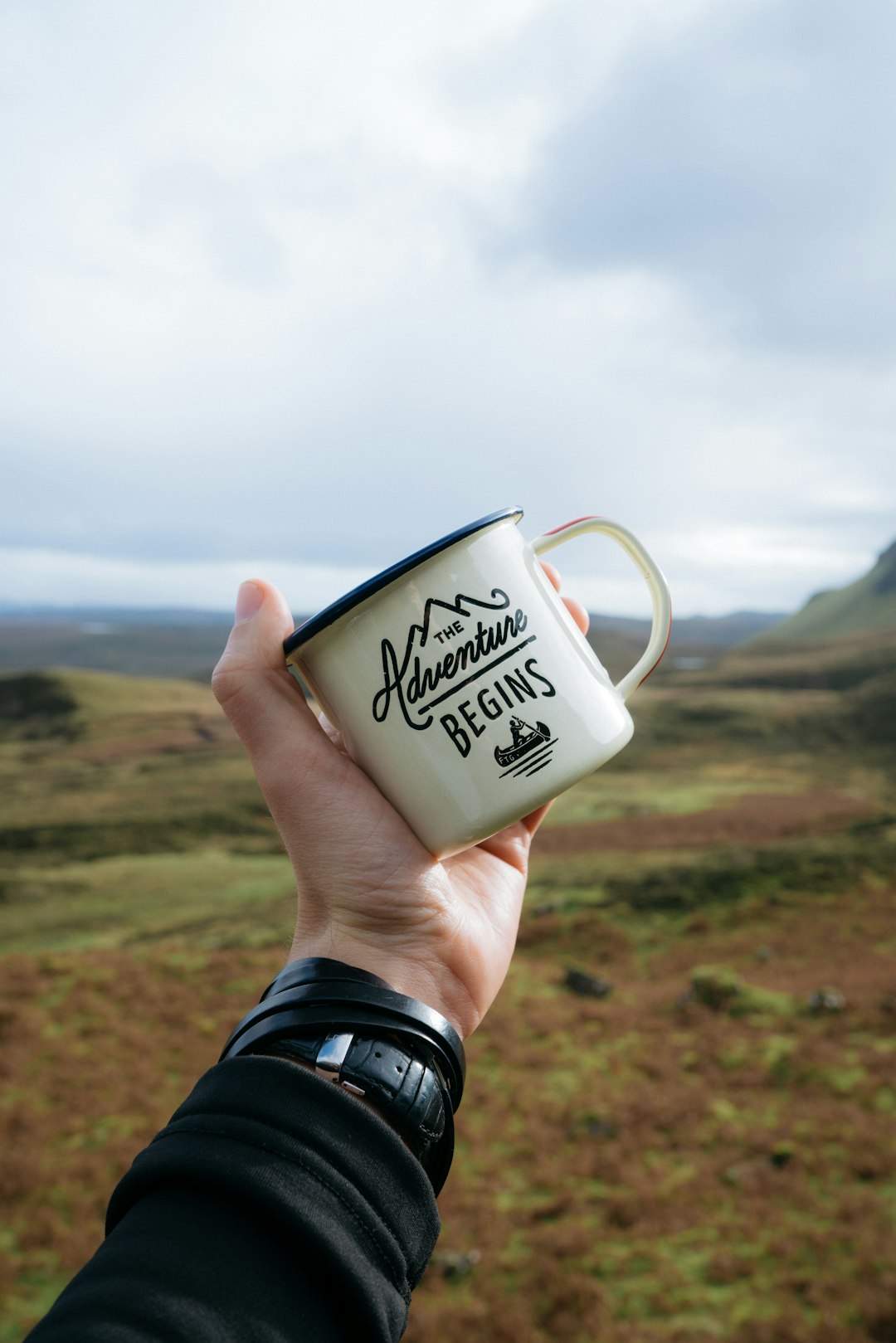 person holding beige and black The Adventure Begins-printed mug during daytime