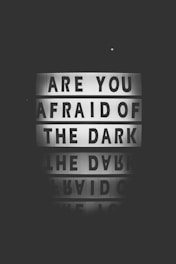 A dark black and white image features a lightbox sign displaying the words 'Are you afraid of the dark' with a reflection of the message below it.