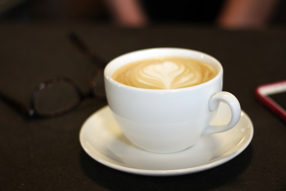 copo de cerâmica branca preenchido com café com leite marrom e branco no pires de cerâmica branca