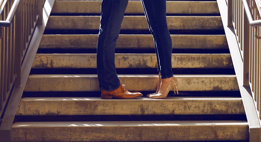 two person wearing blue jeans standing on gray concrete stair
