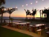 Sunset over a sandy beach with surfboards and handcrafted wooden gifts displayed on a table.