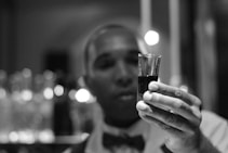 grayscale photo of man holding shot glass filled with liquid