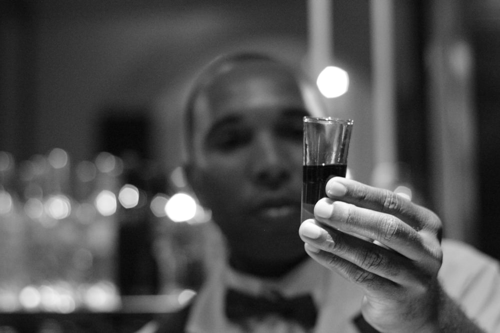Graustufenfoto eines Mannes, der ein mit Flüssigkeit gefülltes Schnapsglas hält