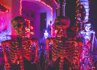 two skeleton near white concrete building with string lights at daytime