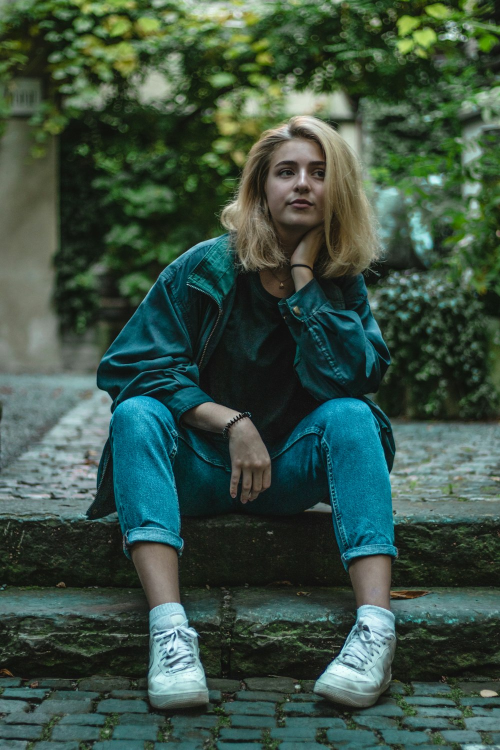 woman in blue denim jacket sits on gray concrete pavement