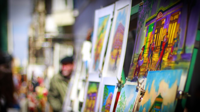 Close-up of colorful oil paintings displayed on easels in an outdoor art festival setting.