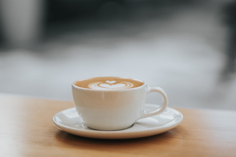 white ceramic teacup filled with coffee latte with saucer on the table photography