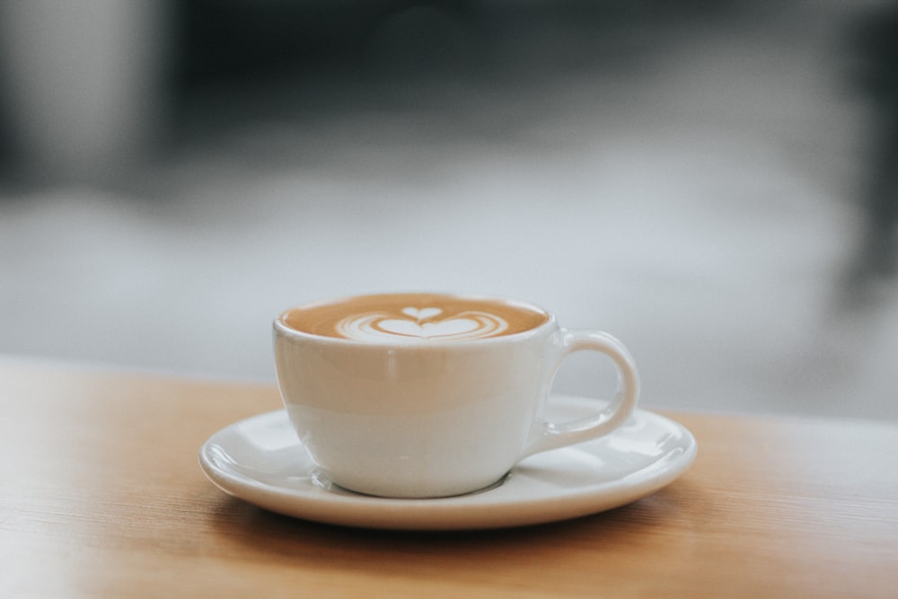 Tazza da tè in ceramica bianca riempita con latte al caffè con piattino sul tavolo fotografia