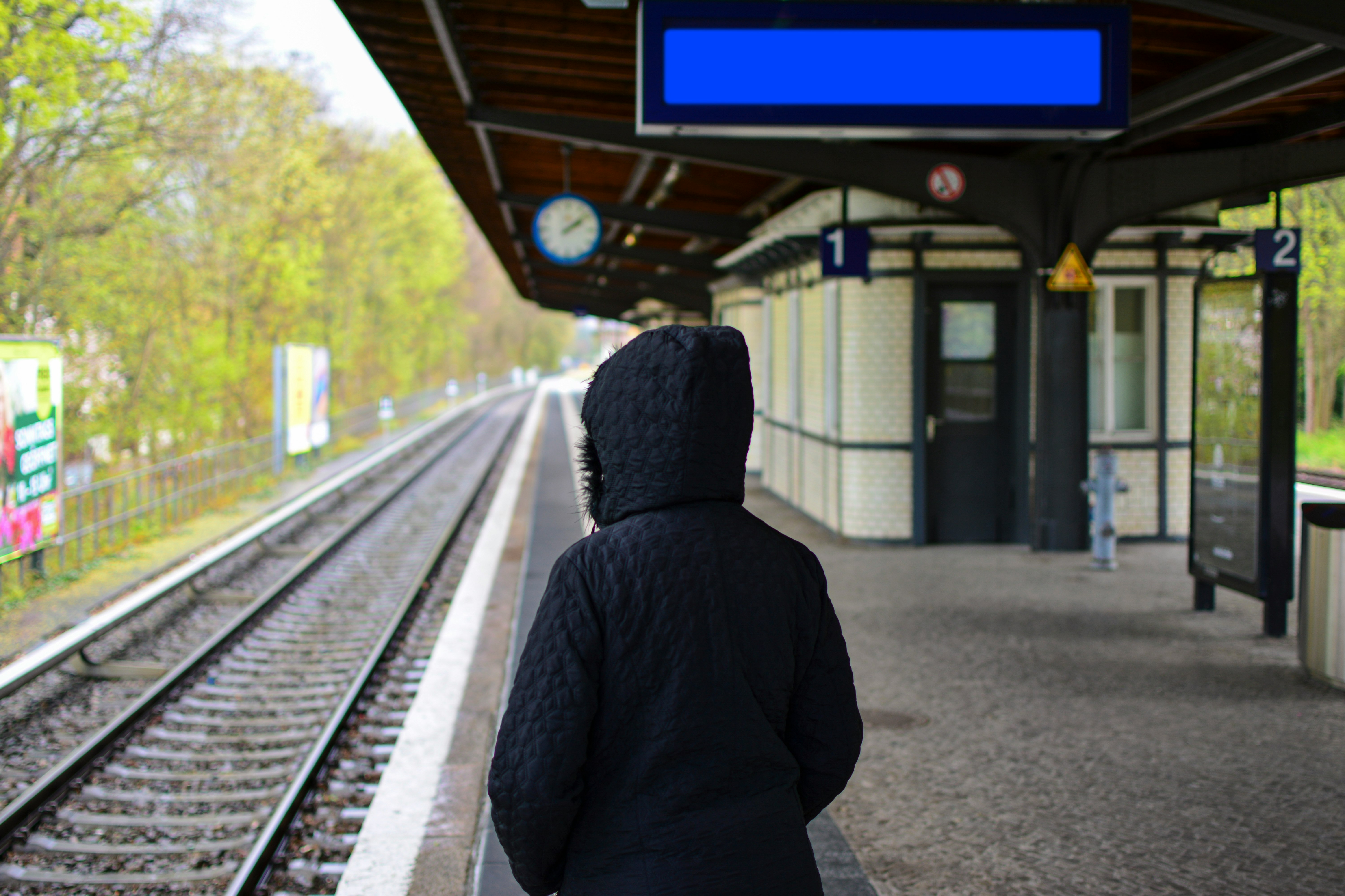 person in hoodie standing near train rail during daytime