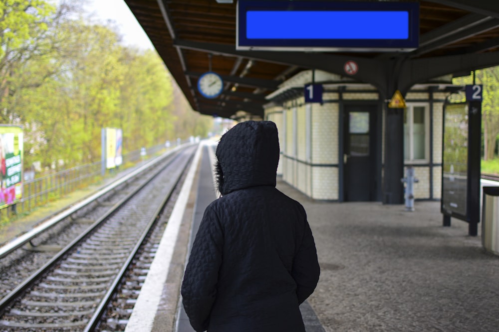 Persona in felpa con cappuccio in piedi vicino alla ferrovia del treno durante il giorno
