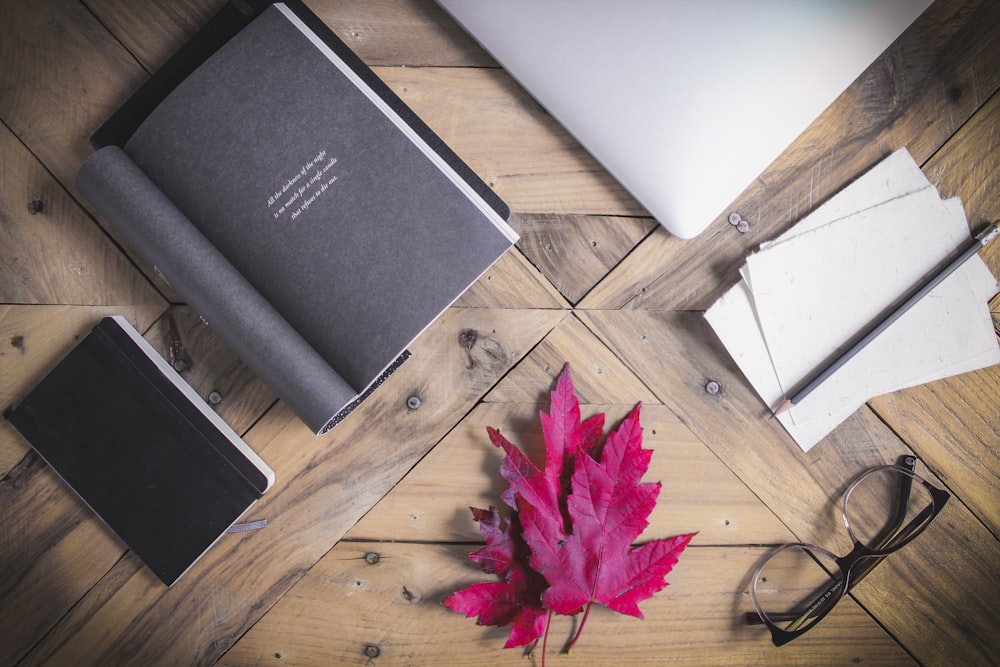 Schwarzes Buch in der Nähe von rosa Ahornblatt auf braunem Holztisch