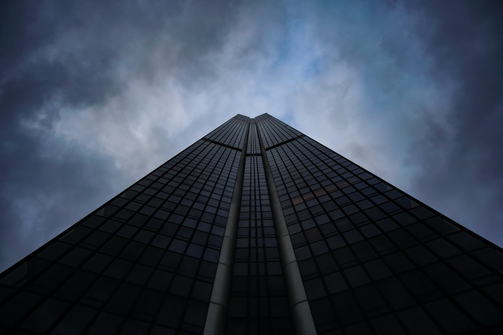low-angle photography of black concrete building with glasses under cloudy sky